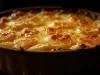 Em cima de uma mesa, refratário redondo com batata e queijo gratinado.