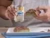 Barra de Dubai, receita de uma barra de chocolate recheada com um creme de pistache e macarrão, decorada com pó dourado e servida em um prato branco com uma pessoa ao fundo segurando metade da receita e a lata de Leite Moça na outra mão