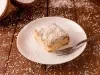 Imagem de um prato branco com um pedaço do bolo coberto com coco e um garfo ao lado.