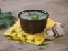 Imagem de um bowl marrom com a receita de caldo verde polvilhada com cebolinha sobre um pano amarelo e chapéus de festa junina ao lado.