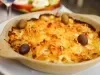 Em cima de uma mesa, refratário redondo com bacalhau gratinado com queijo, decorado com azeitonas pretas e verdes.