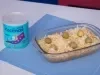 Fotografia de um recipiente refratário de vidro, retangular, ao lado da lata de Ascenda, sobre um paninho azul quadrado. Dentro do recipiente tem a torta com massa de grão de bico e ascenda, finalizada com queijo parmesão e azeitonas.