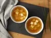 Imagem vista de cima de 2 tigelas brancas com sopa de missoshiro e todu sobre uma tábua preta e pedaços de cebolinha ao lado