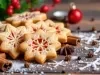 Em cima de uma mesa decorada com enfeites de natal, biscoitos dourados e crocantes em formato de estrela, decorados com confeito de açúcar.