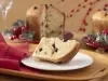 Imagem de uma fatia de panetone caseiro com gotas de chocolate em um prato branco. Ao fundo, o panetone e decorações de Natal.