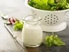 Imagem de um pode de vidro com molho de iogurte, um mini fuet e umas folhas de salada. Ao fundo, um escorredor branco com folhas de alface.