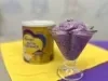 sobre um fundo azul e amarelo e branco está uma taça com um sorvete cremoso roxo cheio de pedacinhos de uva, ao fundo desfocado está uma lata do produto Ninho NutriAdvance em tons de dourado.
