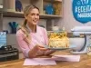 Foto da confeiteira Beca Milano segurando a receita de Bolo de Frutas Amarelas com Merengue, atrás de uma bancada de madeira de cozinha.