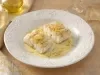 Filés de bacalhau servidos com molho cremoso de ervas e raspas de limão, apresentados em prato branco elegante.