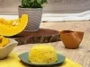 Fotografia em tons de amarelo com um prato azulado ao centro. Em cima do prato existe um pão de cor amarelada feito com abóbora e farinha de aveia. Ao fundo existe uma fatia de abóbora.