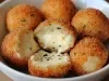 Fotografia de várias bolinhas de queijo crocantes dentro de um recipiente médio e fundo de cor branca. O foco da imagem mostra três metades abertas com o queijo derretido.