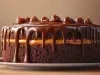 Fotografia de um bolo de chocolate com cobertura cremosa em um prato branco, com uma camada de recheio de doce de leite e coberto por um ganache brilhante que escorre pelas laterais.