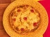 Fotografia mostra uma quiche com queijo gratinado e pedaços de tomate sobre um prato amarelo. Ao fundo, uma mesa de madeira e um pano vermelho.