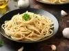 Imagem de um prato preto com macarrão alho e óleo decorado com salsinha.