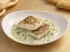 Filé de peixe branco dourado servido no molho cremoso de ervas, apresentado em prato fundo branco com acabamento sofisticado.