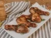 Imagem de coxas de frango douradas feitas na air fryer sobre um prato retangular branco.