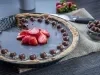 Fotografia de uma torta grande de bombom de morango dentro de uma forma redonda preta. Por cima da ganache da torta temumas bolinhas de chocolate e morangos em pedaços decorando-a. Ao lado tem uma faca e mais bolinhas de chocolate num potinho.