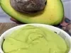 Foto da receita de Mousse de Abacate. Observa-se um potinho branco com a mousse cremosa dentro e um abacate pela metade atrás ilustrando.