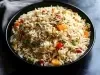 Em cima de uma mesa, tigela redonda com porção de arroz soltinho com pimentões amarelo, vermelho, ervilhas e cenouras picadas.