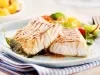 Fotografia mostra dois filés de peixe grelhado sobre um prato branco e salada.