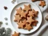 Em cima de uma mesa decoradas enfeites de Natal, prato com biscoitos em formato de estrelas simples.