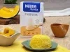 Fotografia em tons de amarelo com um prato azulado ao centro. Em cima do prato existe um pão de cor amarelada feito com abóbora e farinha de aveia. Ao fundo existe uma fatia de abóbora e uma embalagem de Farinha de Aveia Nestlé
