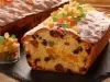 Em cima de uma mesa, bolo fofinho com frutas cristalizadas e uvas-passas, deccorado com frutas cristalizadas.