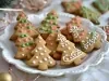 Em cima de uma mesa, prato redondo com biscoitos em formato de árvore de Natal, decorados com glacê branco, verde e rosa.