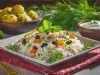 Em um prato quadrado de porcelana, há uma base de arroz soltinho, combinado com pedaços de presunto cozido, coloridos vegetais, como cenoura, uvas-passas e decorado com cebolinha picada.