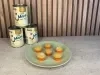 Docinhos claros cobertos com açúcar em forminhas laranja, dispostos em prato verde com Leite Moça ao fundo.