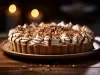 Em cima de uma mesa, banoffee com massa de biscoitos crocante, decorado com chantilly cremoso, polvilhado com raspas de chocolate.