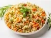 Visto de cima, prato branco redondo com arroz soltinho, cenouras cortadas em cubos, ervilhas e pedaços de cheiro-verde picados.