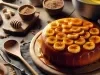 Bolo redondo com fatias de banana organizadas no topo, cobertas por uma calda espessa e brilhante de caramelo. O cenário é rústico, com utensílios de madeira, ingredientes como açúcar mascavo, mel e bananas ao fundo.