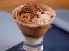 Taça com sorvete de chocolate, raspas por cima e base cremosa, servida sobre tecido azul.