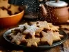 Em cima de uma mesa, prato redondo preto com biscoitos em formato de estrelas, polvilhado com açúcar de confeiteiro.