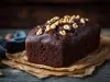 Bolo de chocolate recém-assado, com uma cor rica e escura, coberto com nozes. Ele está sobre papel em uma superfície de madeira rústica.