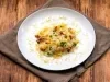 Em um prato branco redondo, porção de arroz com ervilha, pedaços de bacon e batata palha.