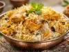 Em cima de uma mesa, prato redondo de metal com arroz soltinho, uvas-passas e frango picado, decorado com folhas de hortelã..