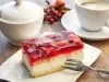 Fotografia de um pedaço de torta de morango em tons claros sobre um praot retangular pequeno branco, apoiado em uma mesa de madeira.