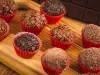 Imagem de brigadeiros gourmet em forminhas vermelhas sobre uma tábua de madeira.
