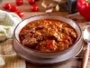 Ensopado de carne macia envolta em um molho avermelhado e espesso, servido em um prato fundo com salsinha picada por cima