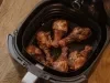 Fotografia em tons de marrom de uma bancada de madeira sobre ela o cesto da airfryer com 6 coxas de frango