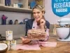 Foto da confeiteira e influenciadora Beca Milano com a receita do Bolo de Baba de Moça com Nozes, decorado com fitas de coco. Ela está atrás de uma balcão de cozinha, com algumas latas de leite Moça e pedaços de coco fresco.