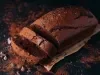 Em cima de uma mesa, bolo de chocolate cortado em duas fatias, polvilhado com cacau em pó.