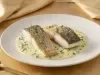 Filé de peixe branco dourado servido no molho cremoso de ervas, apresentado em prato fundo branco com acabamento sofisticado.