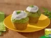 Muffins de espinafre sobre prato amarelo, com cobertura cremosa clara e folhas verdes por cima, dispostos em mesa de madeira.
