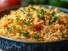 Em cima de uma mesa, tigela com porção de arroz soltinho e cremoso com pimentões e decorado com folha de salsa.