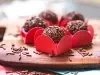Imagem de brigadeiros cobertos com chocolate granulado na forminha vermelha sobre uma tábua de madeira.