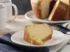 Imagem de um prato branco com um pedaço de bolo branco simples. Ao fundo, um prato com o bolo inteiro.