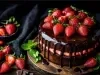 Bolo de chocolate rico, com ganache escorrendo pelas laterais, decorado com morangos inteiros e folhas de hortelã. Colocado em uma tábua de madeira rústica, o bolo é embelezado por morangos e pedaços de chocolate ao redor.